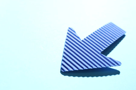 One paper arrow on light blue background, closeup. Space for text
