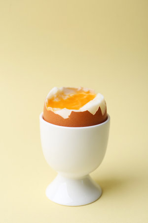 Soft boiled egg in eggcup on beige background, closeup