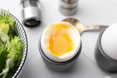 Soft boiled eggs in cups served on white tiled table, closeup
