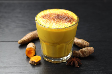 Delicious turmeric latte, powder and rhizomes on black wooden table, closeupの写真素材