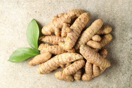 Pile of tumeric rhizomes with leaves on gray table, top view