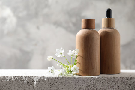 Bottles of cosmetic products and beautiful white flowers on concrete surface against gray background, space for textの写真素材