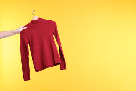 Woman holding hanger with red sweater on yellow background, closeup. Space for textの写真素材