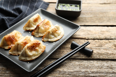 Delicious fried gyoza dumplings with sesame seeds served on wooden table, closeup