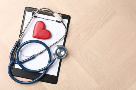 Cardiology. Clipboard, stethoscope and red decorative heart on wooden table, top view. Space for...