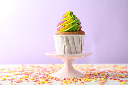 One delicious cupcake with colorful cream and sprinkles on white table against violet background,...