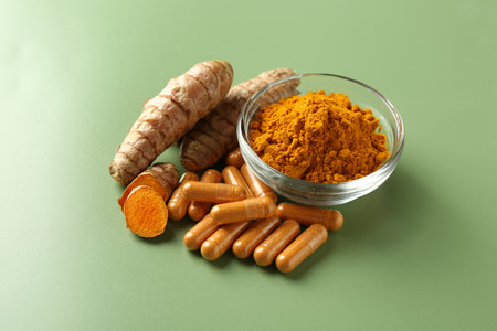 Turmeric powder in bowl, roots and capsules on green backgroundの写真素材