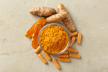 Turmeric capsules, powder and roots on gray table, flat lay