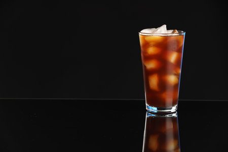 Refreshing iced coffee in glass on black mirror surface. Space for text