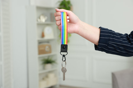 Woman holding key with keychain in LGBT colors indoors, closeupの写真素材