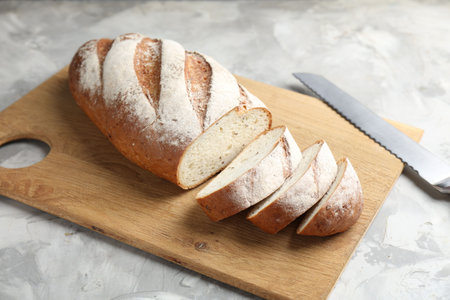 Wooden cutting board with fresh bread and knife on grey table, closeup