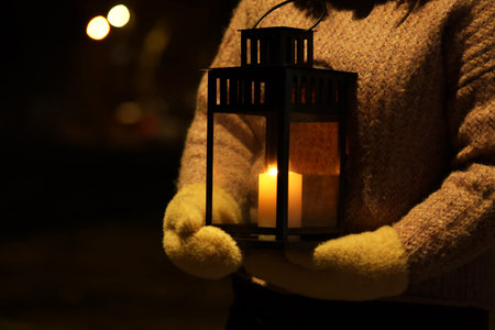 Woman holding Christmas lantern with burning candle in darkness, closeup. Space for textの写真素材