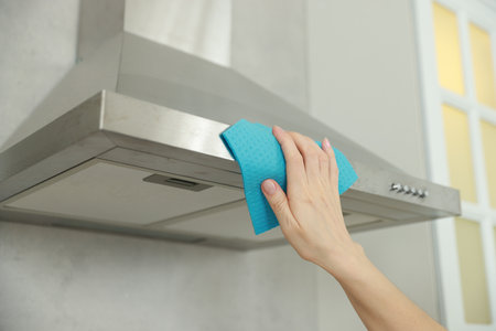 Woman cleaning kitchen hood with rag indoors, closeup