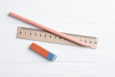 Ruler, pencil and eraser on white wooden table, flat lay