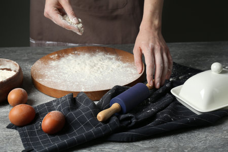 Woman with rolling pin and flour at gray table, closeup