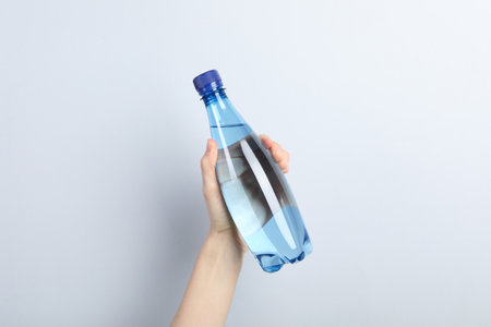 Woman holding plastic bottle of water on light background, closeupの写真素材