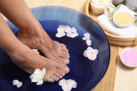 Woman soaking her feet in bowl with water and flowers on floor, closeup. Spa treatmentの写真素材