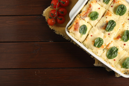 Delicious spinach lasagne in baking dish and fresh tomatoes on wooden table, flat lay. Space for textの写真素材