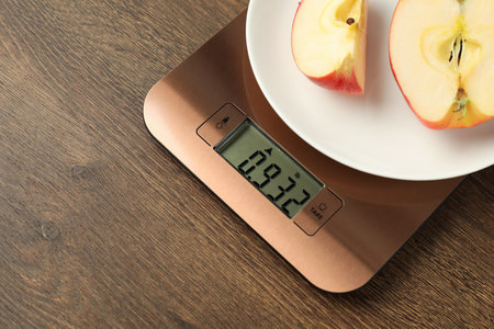 Modern electronic kitchen scale with cut apple on wooden table, closeup. Space for textの写真素材