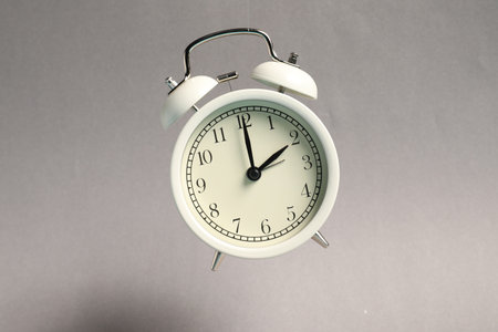White alarm clock in air on light gray background