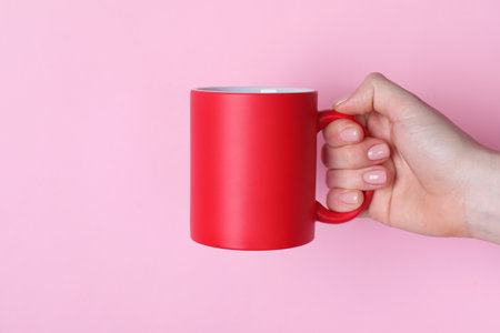 Woman holding blank red mug on pink background, closeup. Mockup for designの写真素材