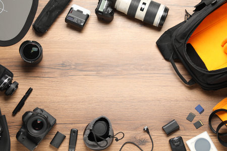 Frame of professional photographer's equipment and backpack on wooden background, flat lay. Space...