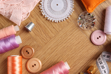 Frame of sewing threads and other supplies on wooden table, flat lay. Space for text
