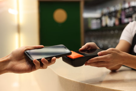 Man paying with smartphone via terminal in cafe, closeup