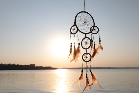 Beautiful handmade dream catcher near river at sunset. Space for text