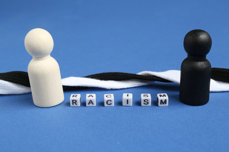Word Racism, human figures and intertwined shoelaces of different colors on blue background, closeup