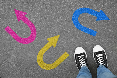 Man standing near colorful arrows pointing in different directions on asphalt road, closeup....