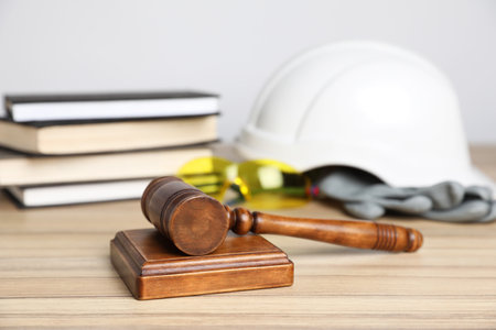 Accident at work concept. Gavel, books and construction worker's protective gear on wooden table, selective focusの写真素材