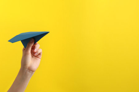 Woman with blue paper plane on yellow background, closeup. Space for textの写真素材