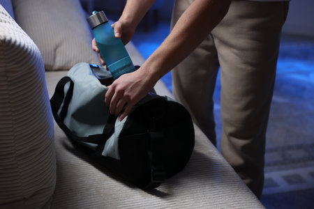Man putting bottle of water into gym bag indoors, closeupの写真素材