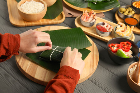 Woman tying banana leaf with food at wooden table with products, closeup. Healthy eco servingの写真素材