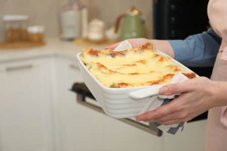 Woman holding baking dish with tasty lasagna in kitchen, closeup. Space for textの写真素材