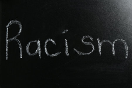 Chalkboard with word Racism as background, top view