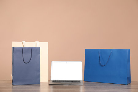 Internet shopping. Laptop and colorful paper bags on wooden table against brown backgroundの写真素材
