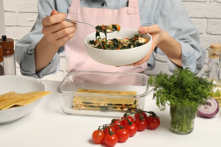 Woman making spinach lasagna at white table indoors, closeupの写真素材