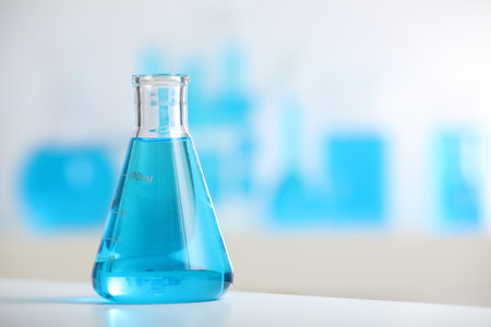 Conical flask with blue liquid on table indoors, closeup. Space for textの写真素材
