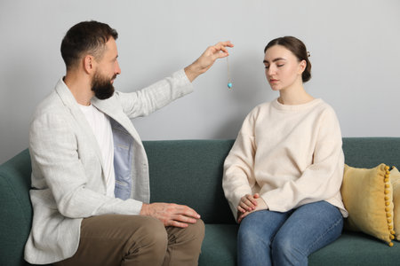 Psychologist using pendulum while working with patient during hypnosis session indoors