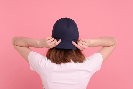 Woman in stylish baseball cap on pink background, back view. Mockup for designの写真素材