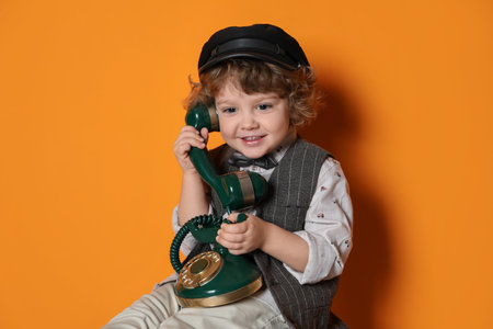 Cute little boy with old telephone on orange backgroundの写真素材