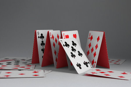 Collapsed house of playing cards on grey background, closeup