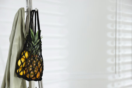 Macrame bag with fruits and jacket on clothing rack near white wall. Space for textの写真素材