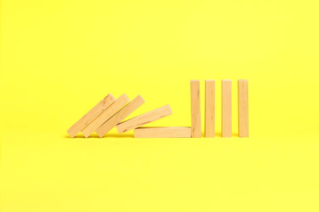 Domino effect. Wooden blocks falling on yellow background. Space for text