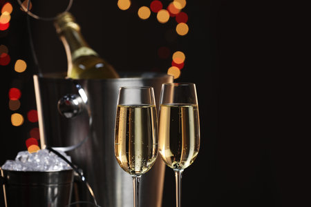 Champagne in glasses, bottle and ice buckets on black background with blurred lights, space for textの写真素材