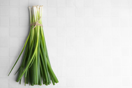 Bunch of fresh green onions on white tiled table, top view. Space for text