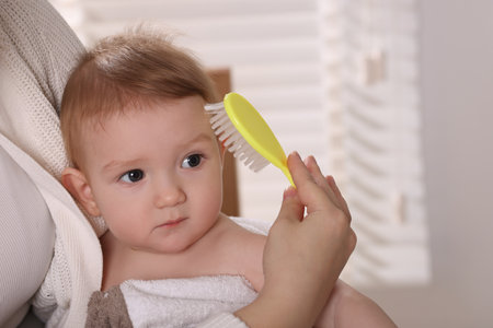 Woman brushing hair of her little baby indoors, closeup. Space for textの写真素材