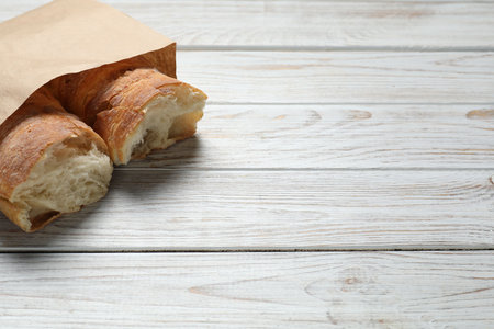 Paper bag with halves of fresh baguette on wooden table, space for textの写真素材
